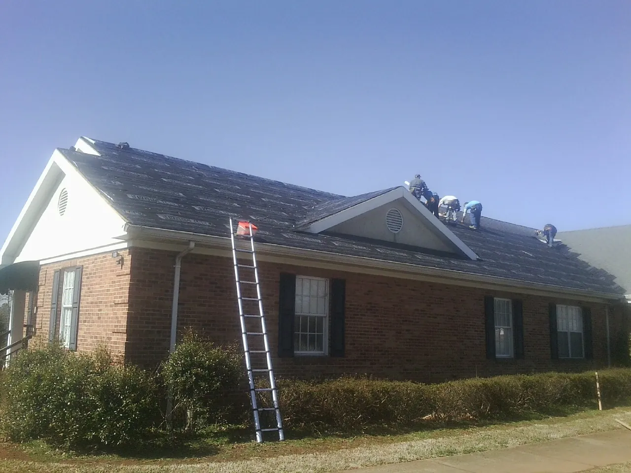 Crew tearing shingles off a brick ranch roof with a ladder set — Emergency Roof Repair work by our crew in Jamestown